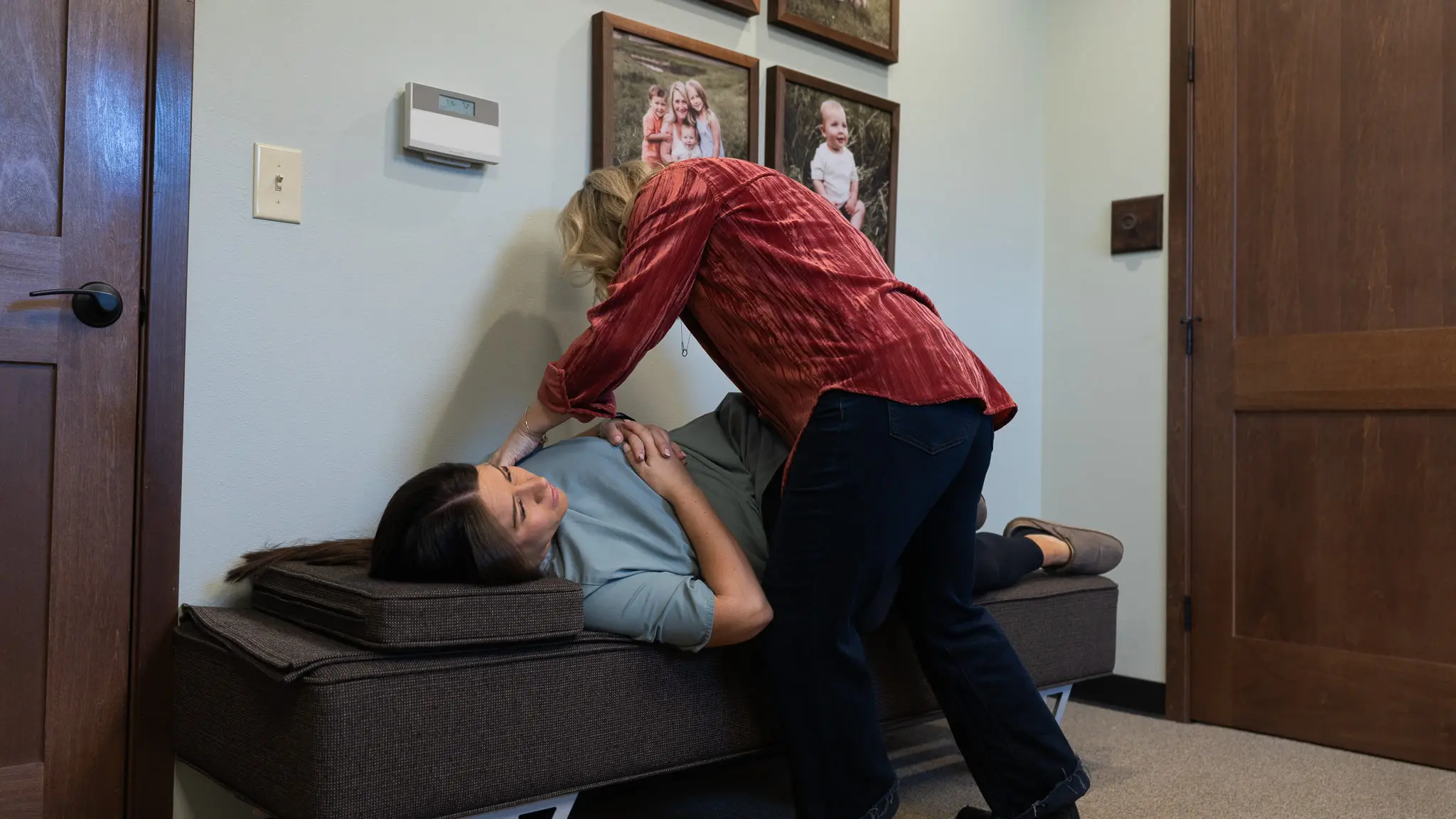 A practitioner in a red shirt performs an adjustment on a patient lying on a treatment bench.
